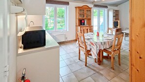 A kitchen with a built-in stove, a dining table with chairs, a wooden cabinet, and a television. - 2 bedroom awesome home in Bredene (Bredene)