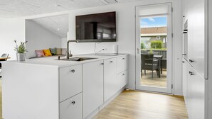 A modern kitchen with white cabinetry, a built-in sink, and a large window overlooking a patio area. - 2 bedroom cozy home in Juelsminde (Juelsminde)