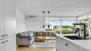 A modern kitchen with a built-in island, a dining area with a round table, and a sofa. - 2 bedroom cozy home in Juelsminde (Juelsminde)