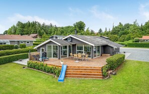 Ett modernt hus med en veranda, stora fönster och en skorsten.