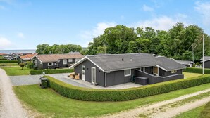 A modern building with a grey exterior, surrounded by well-maintained hedges and a gravel path. - 2 bedroom cozy home in Juelsminde (Juelsminde)