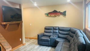 A living room with a sectional sofa, a mounted flat-screen TV, and a fish wall art piece. - VRBO unit in private home, in town with ocean views (Homer)