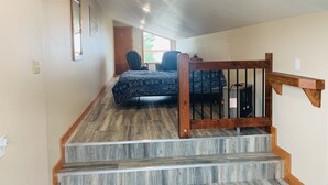 A bedroom with a bed, a chair, and a staircase with wooden railings. - VRBO unit in private home, in town with ocean views (Homer)