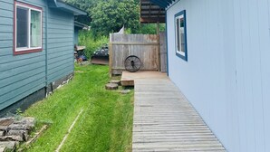A covered wooden deck leading to a house with a blue exterior. - VRBO unit in private home, in town with ocean views (Homer)