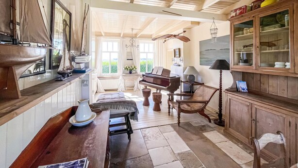 Una habitación amplia con un piano de cola, muebles de madera y un gran ventanal con vistas a la vegetación.