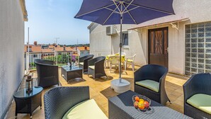 A sunlit outdoor patio with wicker furniture, a table with fruit, and a large umbrella.