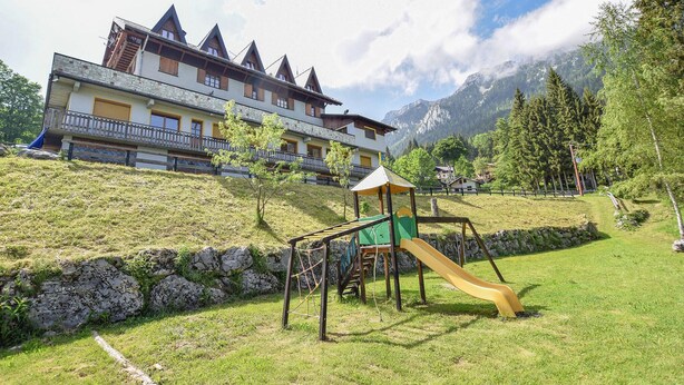 A hotel with a play area, including a slide, set against a backdrop of mountains and trees. - Gorgeous apartment in Lamon with WiFi (Lamon)