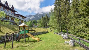 A playground with a slide and climbing structure, surrounded by a wooden fence, with houses and mountains in the background. - Gorgeous apartment in Lamon with WiFi (Lamon)