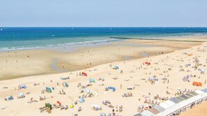 Ein weiter Sandstrand mit vielen Sonnenschirmen und Liegen, ein klarer Himmel und ruhiges Meer.