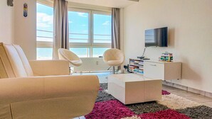 Ein modernes Wohnzimmer mit Sofa, zwei Sesseln, Couchtisch, Fernseher und Bücherregal.