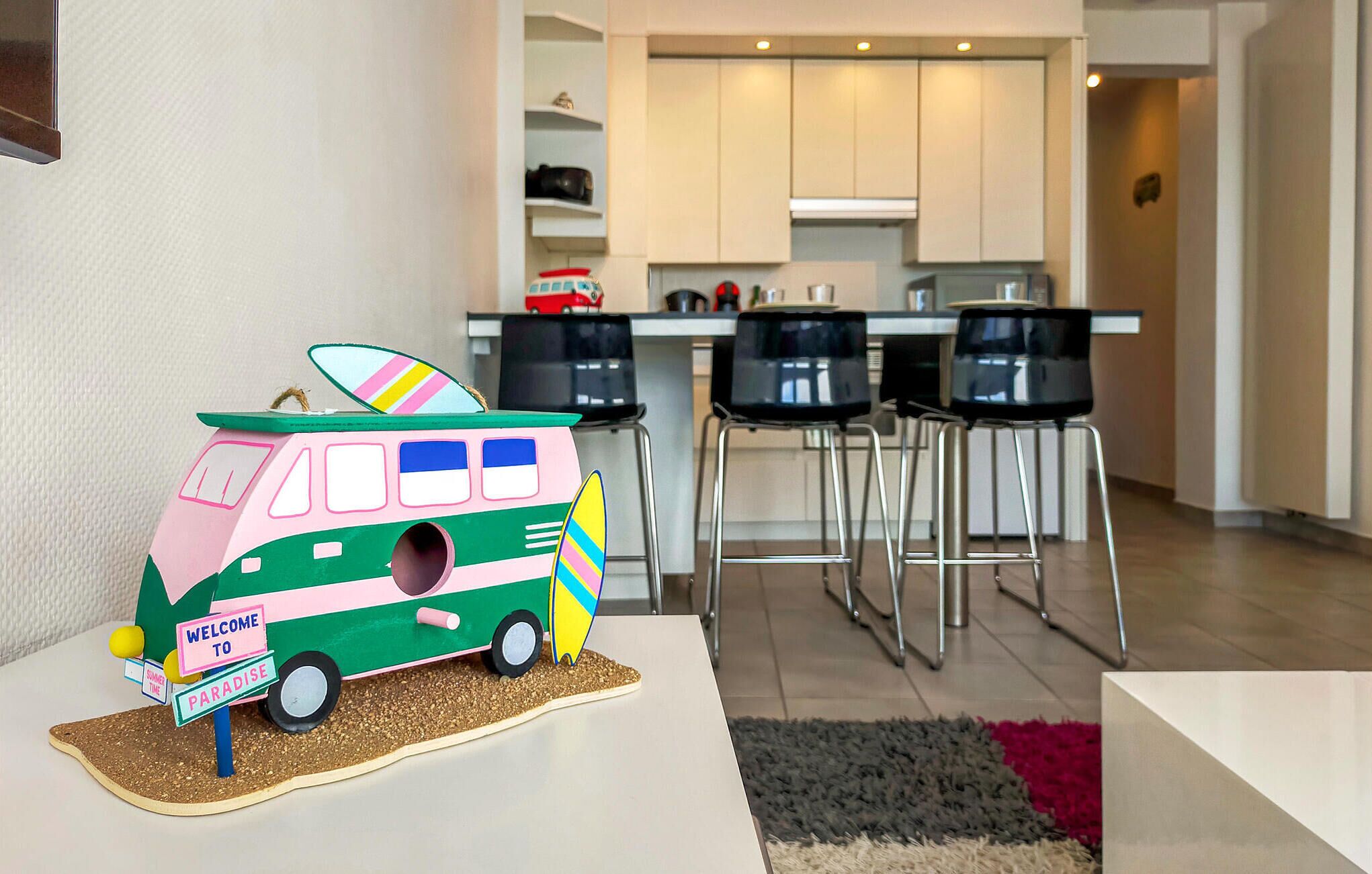 A modern kitchen with white cabinets, black chairs, and a colorful van decoration.