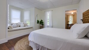 Quarto com uma cama grande, um assento junto à janela com almofadas, um tapete redondo de fibra natural e uma luminária no teto.