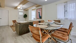 Uma sala de jantar com mesa de vidro, jogos americanos trançados e cadeiras de metal.