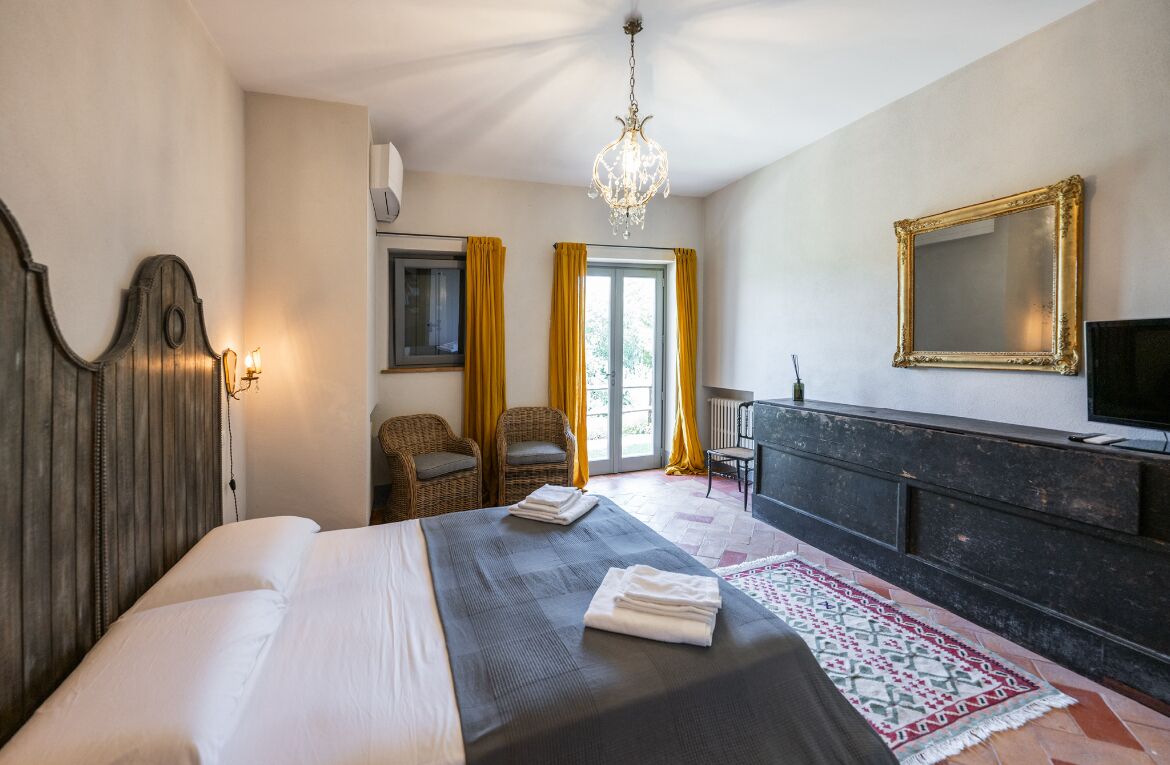 A hotel room with a large bed, a television, a chandelier, and a view of the outdoors.