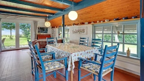 Un coin repas avec une table dressée pour quatre personnes, entourée de chaises bleues, sous un plafond en bois avec des poutres apparentes.