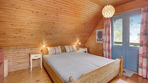Une chambre confortable avec un plafond en bois, un lit agrémenté d’un coussin à rayures, des lampes de chevet et une fenêtre avec des rideaux.