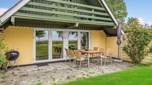 Une terrasse couverte avec une table et des chaises, un barbecue et une vue sur la mer, visible à travers des portes vitrées.