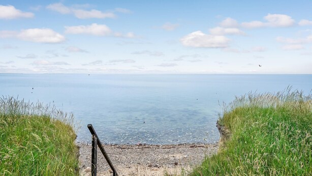 Une vue dégagée sur une plage, avec un poteau en bois au premier plan et une mer calme à l’arrière-plan.