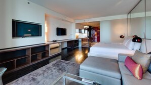 A modern hotel room with a flat-screen TV, a sofa, a bed, and a dining area.