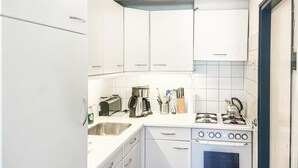 A compact kitchen with white cabinets, a sink, a toaster, a coffee maker, a kettle, and a stove. - Beautiful (sta)caravan in Bergen aan Zee with WiFi (Bergen aan Zee)