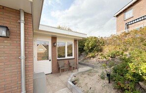 A residential property with a brick facade, a front door, a small porch with two chairs, and a garden area with plants and a stone pathway. - Beautiful (sta)caravan in Bergen aan Zee with WiFi (Bergen aan Zee)