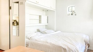 A bedroom with a bed, a bedside table, a wardrobe, and a small window with a plant. - Beautiful (sta)caravan in Bergen aan Zee with WiFi (Bergen aan Zee)