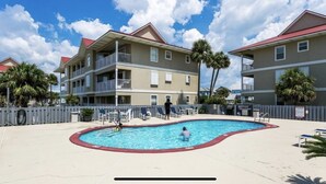 A swimming pool area with a pool, lounge chairs, and a building with balconies. - Beautifully Remodeled Bay Front Condo (Navarre)