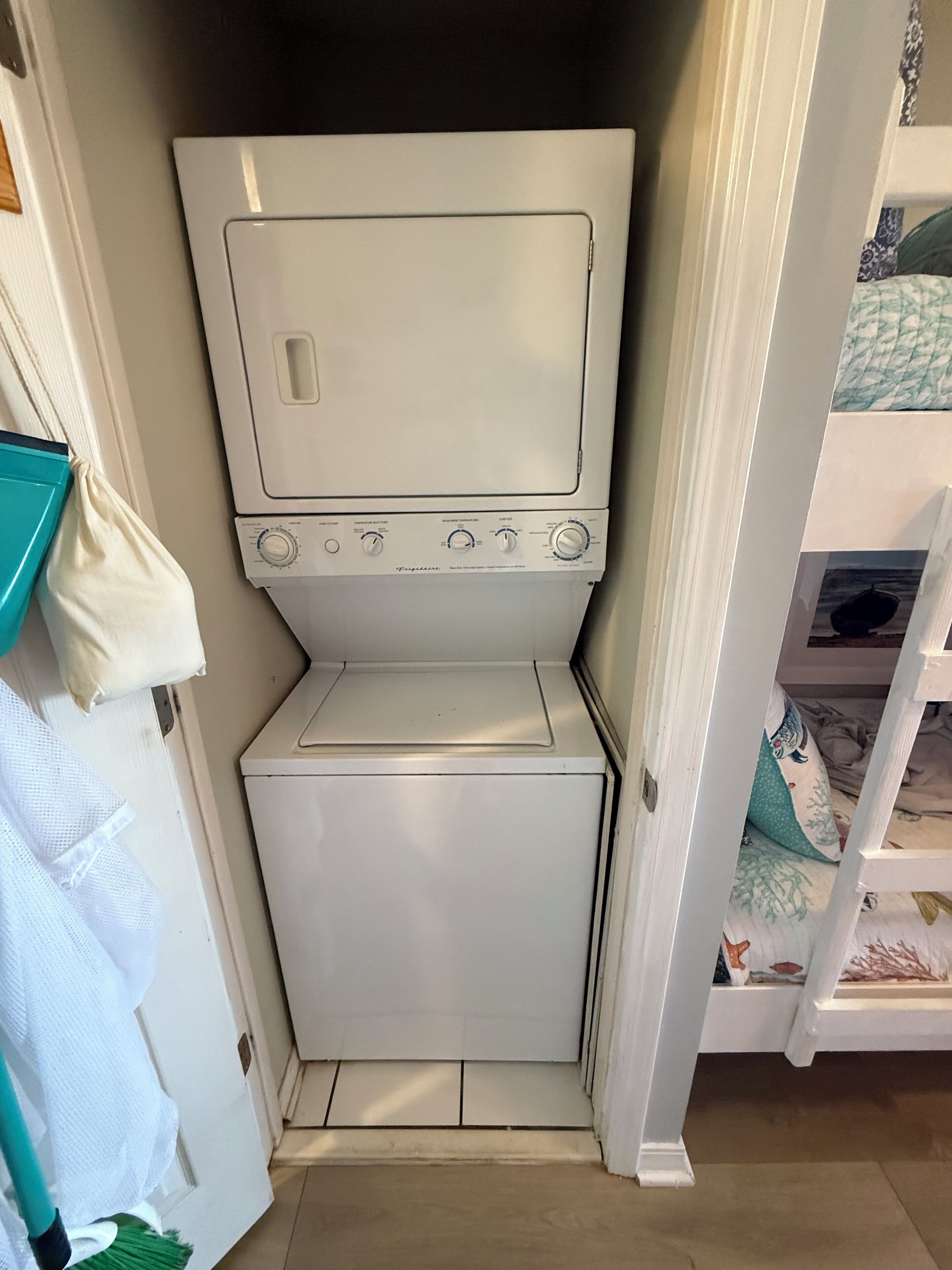 Une petite buanderie comprenant un lave-linge et un sèche-linge, une petite marche et une porte donnant sur une chambre avec un lit superposé.