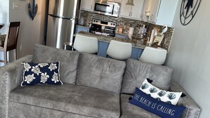A grey sectional sofa with two decorative pillows, a wooden floor, and a kitchen area in the background. - Beautifully Remodeled Bay Front Condo (Navarre)