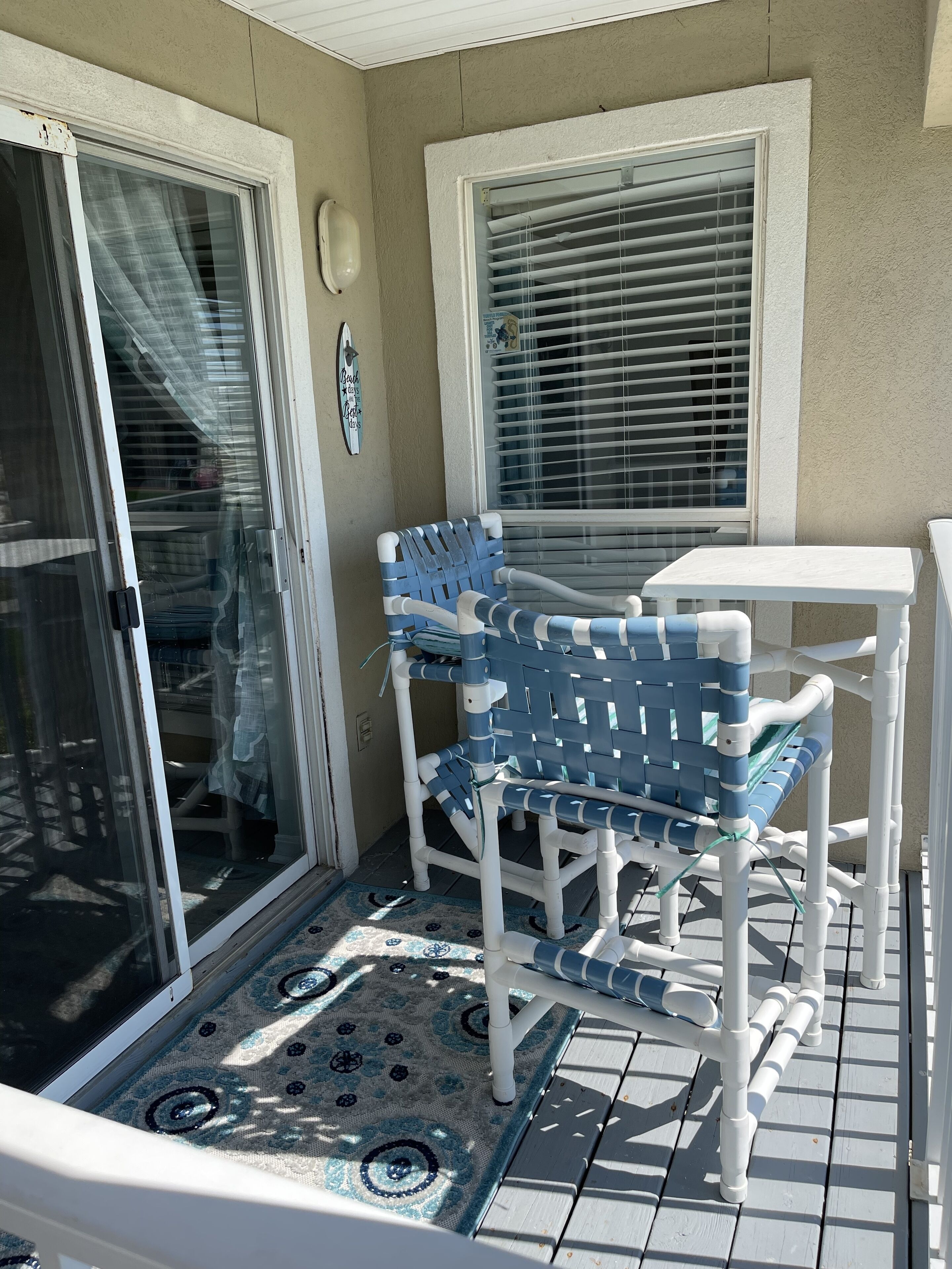 Eine Terrasse mit einem weißen Tisch und blauen Stühlen, einem gemusterten Teppich und einer Schiebetür.