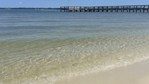 A beach with clear water, a sandy shore, and a pier extending into the water. - Beautifully Remodeled Bay Front Condo (Navarre)