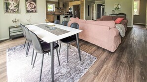 Un espace de vie moderne comprenant un coin repas, un canapé rose et une cuisine en arrière-plan.