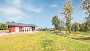 Un bâtiment rouge doté d’un porche couvert et d’un drapeau, entouré d’une pelouse et d’arbres.