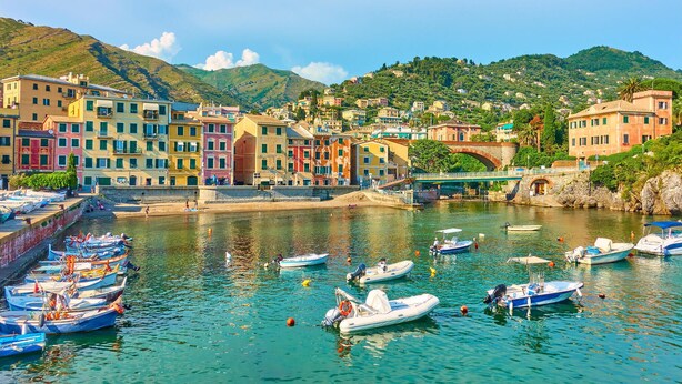 A coastal town with colorful buildings, a bridge, and boats docked along the waterfront.