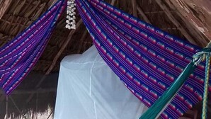 A thatched-roof hut with a bed covered by a white sheet and a colorful hammock. - Cenote Pueblo Fantasma (Chemax)