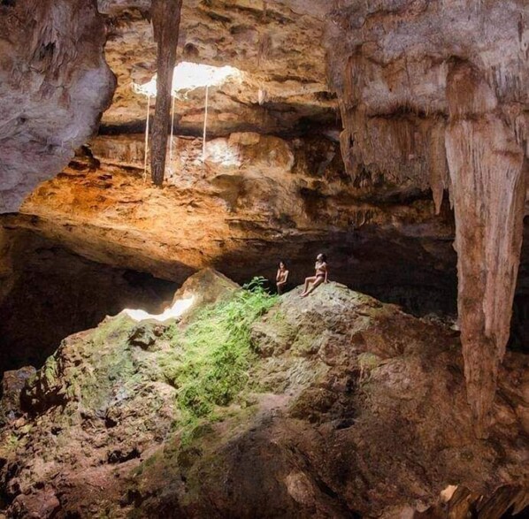 A cave with stalactites and stalagmites, two people sitting on a rock formation, and a light source illuminating the cave.