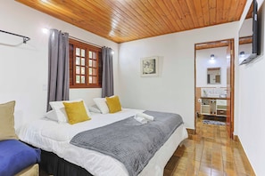 Een slaapkamer met een bed, gordijnen, een raam, een spiegel en een badkamer die door een open deur zichtbaar is.