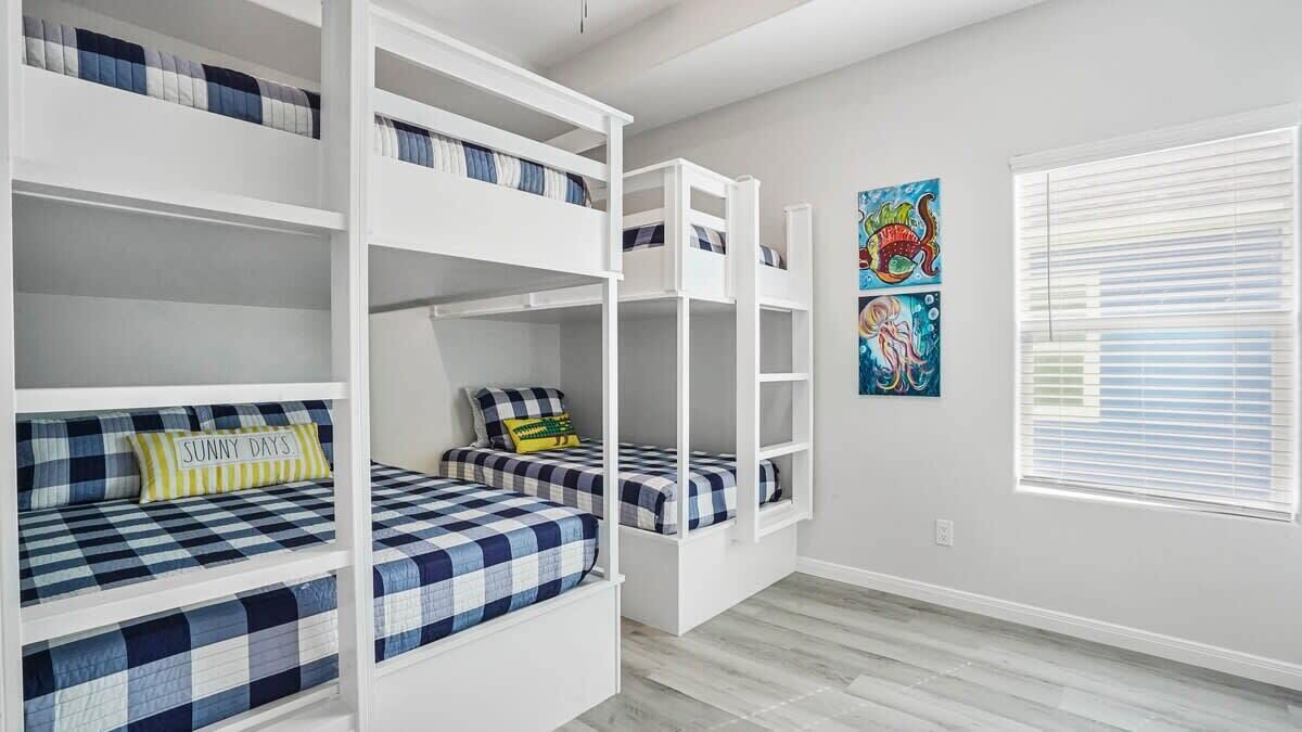 A room with bunk beds, a window with blinds, and two colorful wall art pieces.