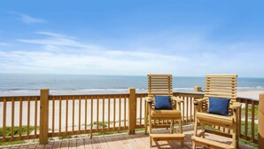 A wooden deck with two wooden chairs and a railing overlooking a beach. - Beachfront Home•Steps to Sand•Sleeps 10 (Bolivar Peninsula)
