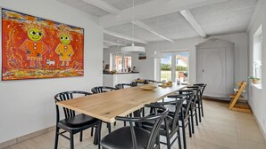 A spacious dining area with a long wooden table and black chairs, a large painting on the wall, and a view of the outdoors through a glass door. - Lovely home in Vestervig with sauna (Vestervig)