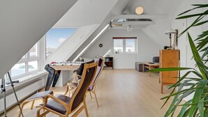 A spacious loft with a high ceiling, a dining area with a table and chairs, a small kitchenette, and a large window offering a view of the sky. - Lovely home in Vestervig with sauna (Vestervig)