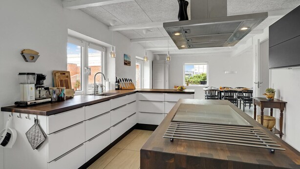 A modern kitchen with white cabinets, a wooden countertop, and a central island with a built-in stove. - Lovely home in Vestervig with sauna (Vestervig)