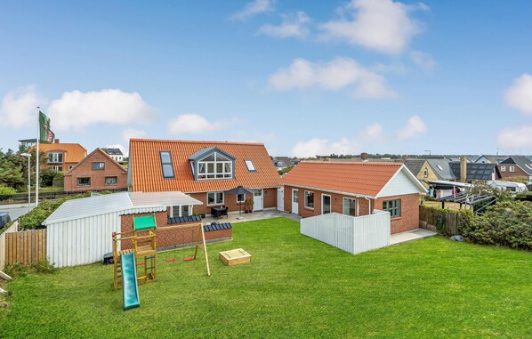 A residential house with a sloped roof, a fenced backyard, and a small play area with a slide and swings. - Lovely home in Vestervig with sauna (Vestervig)