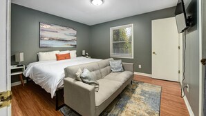 Ein Schlafzimmer mit einem Bett, einem Schlafsofa, einem Fernseher und einem Fenster mit Jalousien.