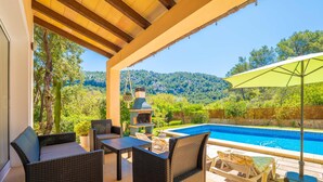 Un patio cubierto con mobiliario de mimbre, una piscina y vistas a un paisaje montañoso.