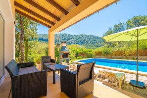 Un patio cubierto con mobiliario de mimbre, una piscina y vistas a un paisaje montañoso.