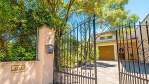 Una entrada protegida por un portón metálico, un letrero que dice 'Villa Garbasso', y un edificio con fachada amarilla al fondo.