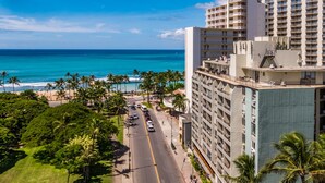 Un hotel con vista al océano, una calle con coches y palmeras.