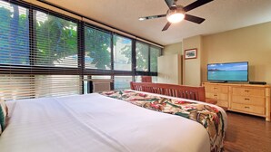 Un dormitorio con cama, ventilador de techo, televisión y vistas al exterior a través de la ventana.