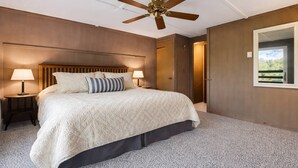 Ein Schlafzimmer mit einem Bett, zwei Nachttischen mit Lampen, einem Deckenventilator, einem Kleiderschrank und einem Fenster mit Blick.